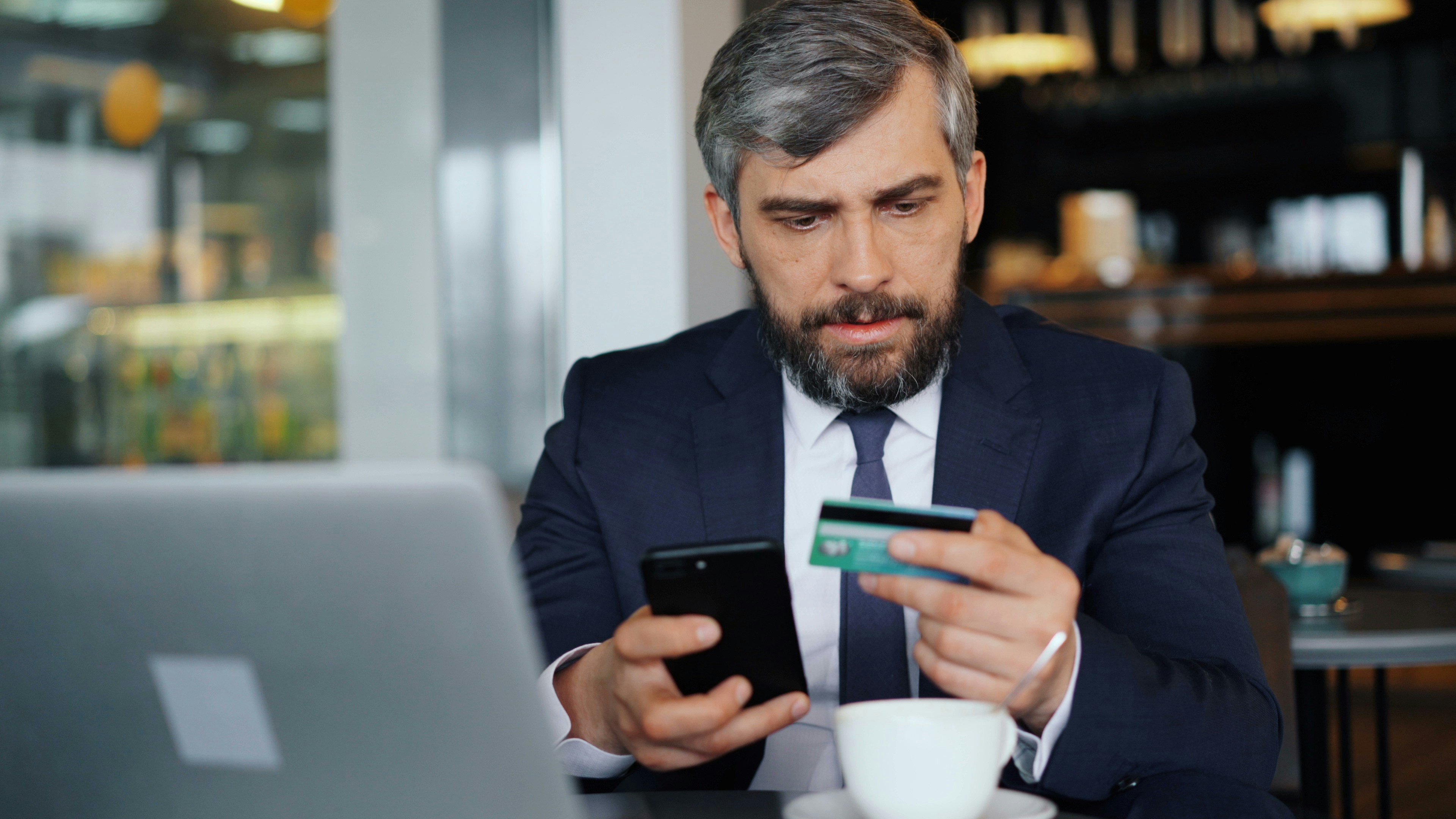 A close-up of a man holding a credit card looking skeptically at a smartphone